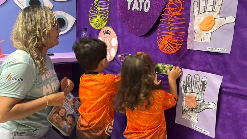 Crianças explorando um painel sobre os sentidos com uma educadora na FICE